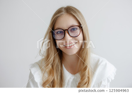 Young woman with glasses smiles warmly while sitting against a light background in a bright indoor space 125984963