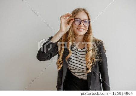 Young woman with long hair wearing glasses and a striped shirt poses confidently in a black blazer indoors 125984964