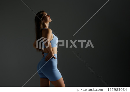 Fitness model posing confidently in workout attire against a dark backdrop emphasizing strength and determination 125985084
