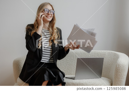 Young professional multitasking in modern office setting during daytime with papers and laptop Young professional multitasking in modern office setting during daytime with papers and laptop 125985086