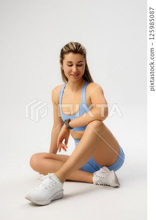 Fitness enthusiast engaging in a supportive stretch in a light blue outfit at a studio during a workout session 125985087