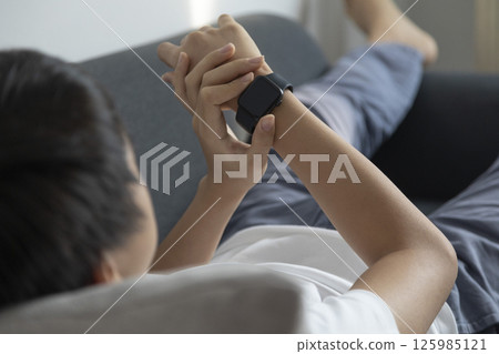 Relaxed weekend. Charming pre-teen boy lying on the sofa with smart watch. 125985121