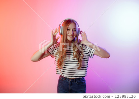 Young woman enjoys music with headphones in a colorful studio setting during a vibrant indoor photoshoot 125985126