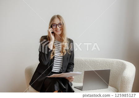 Businesswoman engages in a phone conversation while sitting on a couch in a modern office setting 125985127