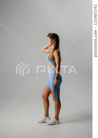 Fitness enthusiast poses in stylish athletic wear showcasing wellness and confidence in a minimalist studio environment 125985142