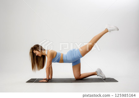 Fitness enthusiast performs leg lift exercise on mat in bright studio setting during daytime Fitness enthusiast performs leg lift exercise on mat in bright studio setting during daytime 125985164
