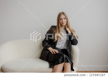 Young professional woman sitting thoughtfully on a cozy couch in a minimalist room during daytime Young professional woman sitting thoughtfully on a cozy couch in a minimalist room during daytime 125985167