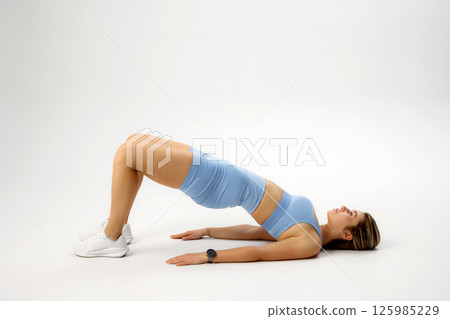 Woman practicing glute bridge exercise on a white background for fitness and strength training 125985229