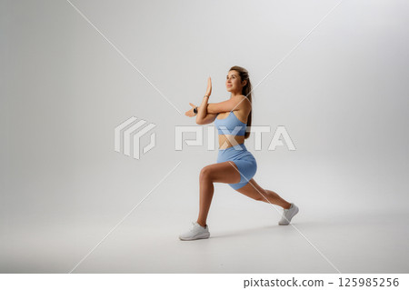 Woman performing a dynamic lunge exercise in a minimalistic studio setting during a fitness session Woman performing a dynamic lunge exercise in a minimalistic studio setting during a fitness session 125985256