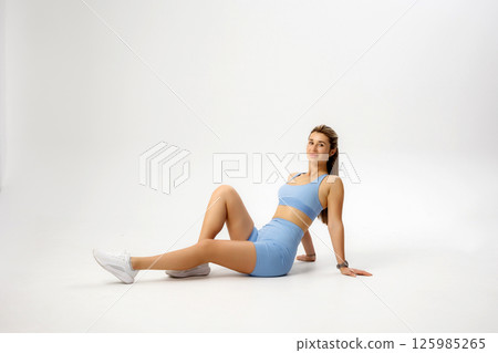 Model in light blue athletic wear poses on a plain background showcasing fitness style and relaxation 125985265