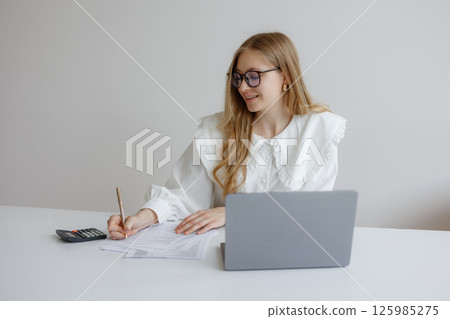 Professional woman working on financial documents at a desk during daytime in a modern office Professional woman working on financial documents at a desk during daytime in a modern office 125985275