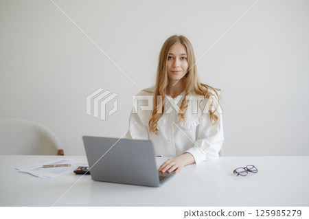 Young woman working on laptop at a modern desk in a bright office space during the day Young woman working on laptop at a modern desk in a bright office space during the day 125985279