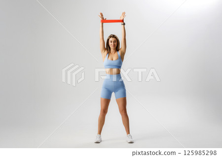 Woman performing a resistance band exercise for upper body strength in a bright studio Woman performing a resistance band exercise for upper body strength in a bright studio 125985298