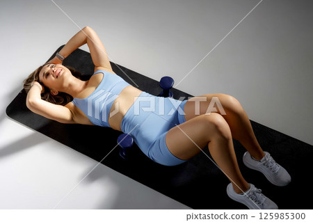 Fitness enthusiast performs abdominal workout on exercise mat in bright studio focusing on strength and health improvement 125985300