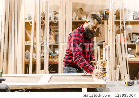 Skilled carpenter using a router to craft wooden panels in a well-equipped workshop environment 125985307