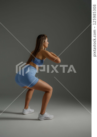 Fitness enthusiast performs squats in a minimalist studio during a workout session wearing athletic gear Fitness enthusiast performs squats in a minimalist studio during a workout session wearing athletic gear 125985308