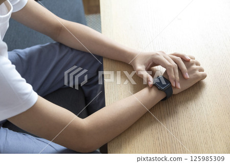 business, technology and people concept - close up of male hand wearing watch at wooden table 125985309