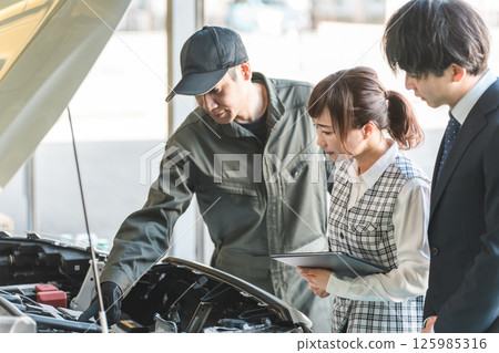 A mechanic giving an explanation in the engine room of a car and staff at a maintenance shop listening to him A mechanic giving an explanation in the engine room of a car and staff at a maintenance shop listening to him 125985316