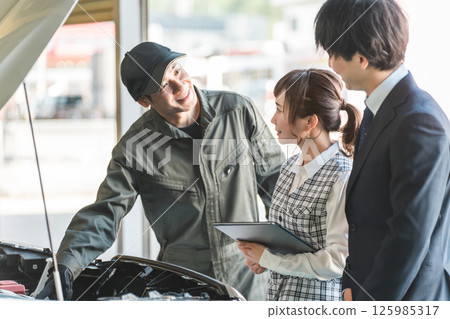 A mechanic giving an explanation in the engine room of a car and staff at a maintenance shop listening to him A mechanic giving an explanation in the engine room of a car and staff at a maintenance shop listening to him 125985317