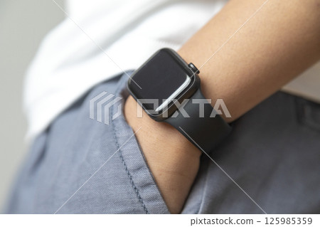 man putting his hand in his jeans pants pocket, wearing a smart watch. Technology. Trees on background. Smart gadget concept. man putting his hand in his jeans pants pocket, wearing a smart watch. Technology. Trees on background. Smart gadget concept. 125985359