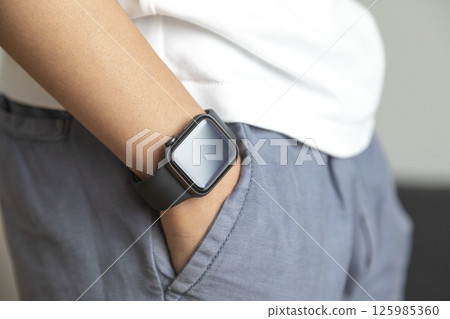 man putting his hand in his jeans pants pocket, wearing a smart watch. Technology. Trees on background. Smart gadget concept. 125985360