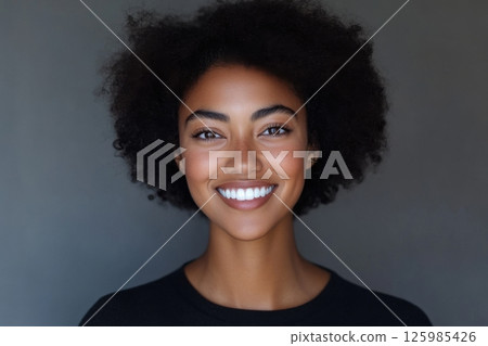 Smiling woman with curly hair poses against a neutral background in a warm, inviting portrait Smiling woman with curly hair poses against a neutral background in a warm, inviting portrait 125985426