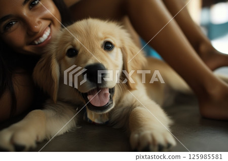 Smiling woman enjoys playful moment with golden retriever puppy indoors during sunny afternoon 125985581