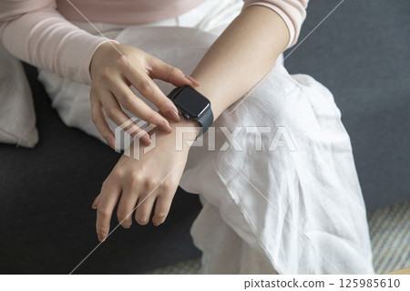 young woman using touchscreen smart watch sitting on sofa at Home. mixed race asian chinese model. 125985610