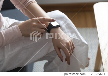 young woman using touchscreen smart watch sitting on sofa at Home. mixed race asian chinese model. young woman using touchscreen smart watch sitting on sofa at Home. mixed race asian chinese model. 125985611