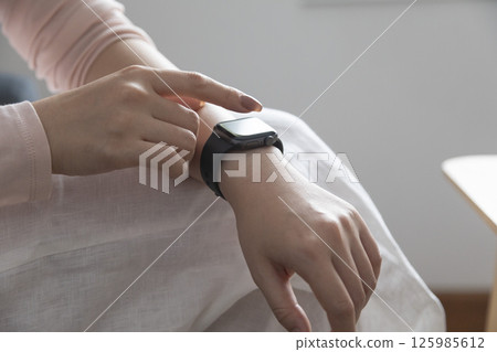 young woman using touchscreen smart watch sitting on sofa at Home. mixed race asian chinese model. 125985612