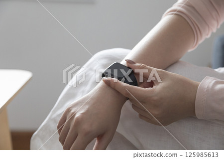 young woman using touchscreen smart watch sitting on sofa at Home. mixed race asian chinese model. 125985613