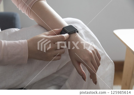 young woman using touchscreen smart watch sitting on sofa at Home. mixed race asian chinese model. young woman using touchscreen smart watch sitting on sofa at Home. mixed race asian chinese model. 125985614