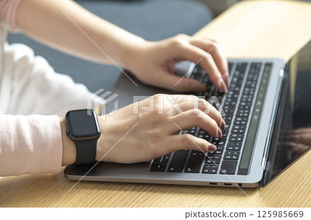 Work from home, Happy Asian young businesswoman use hand finger touch screen modern laptop computer she wears a smart watch on the wrist focus on smartwatch 125985669
