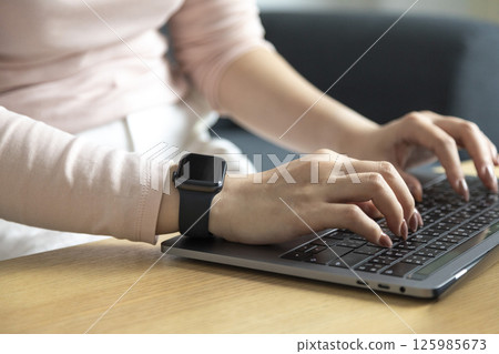 Work from home, Happy Asian young businesswoman use hand finger touch screen modern laptop computer she wears a smart watch on the wrist focus on smartwatch 125985673