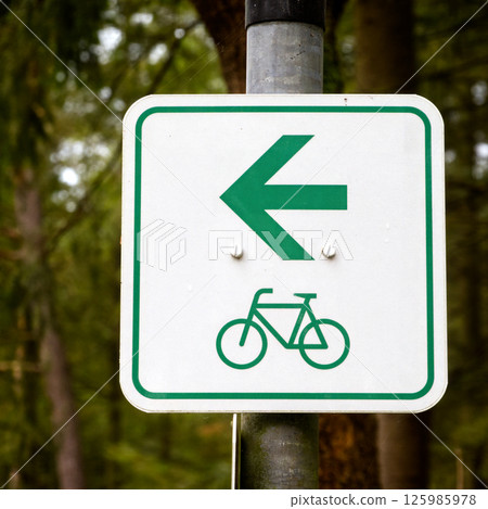 Bicycle lane sign showing left arrow direction in a forest Bicycle lane sign showing left arrow direction in a forest 125985978