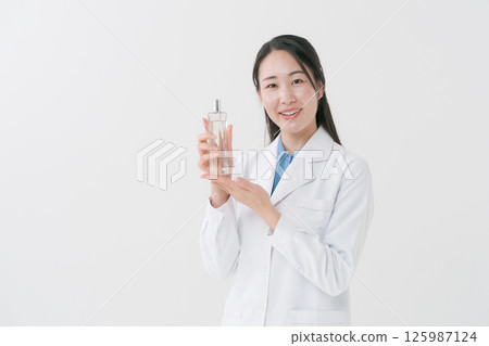 一位身穿白大褂的女士手裡拿著一瓶乳液 125987124