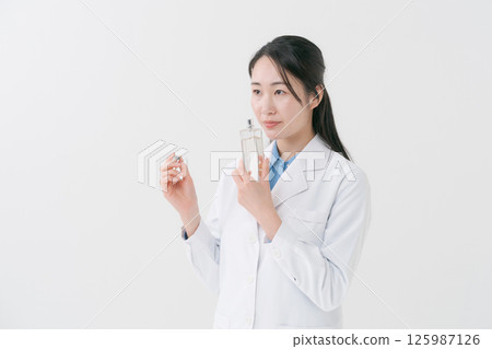 一位身穿白大褂的女士手裡拿著一瓶乳液 一位身穿白大褂的女士手裡拿著一瓶乳液 125987126