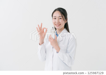 一位身穿白大褂的女士手裡拿著一瓶乳液 125987129