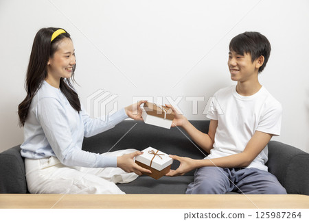 Excited, surprised woman receiving gift box from man sitting on a couch in the living room at home. Excited, surprised woman receiving gift box from man sitting on a couch in the living room at home. 125987264