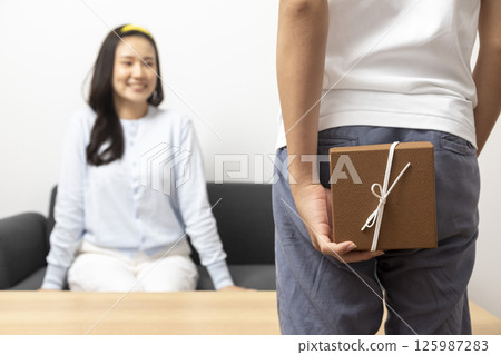 Guy is holding gift behind him is trying to surprise his is waiting girlfriend at home. Focus on boy. Guy is holding gift behind him is trying to surprise his is waiting girlfriend at home. Focus on boy. 125987283