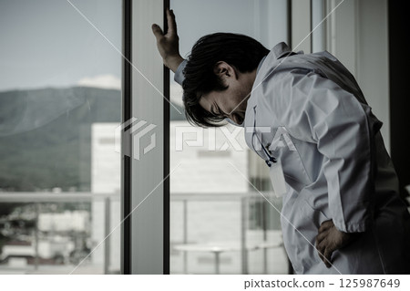 男醫生靠在玻璃窗上（壓力、過度勞累、疲勞、擔心、思考） 125987649