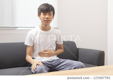 eautiful boy wearing casual  t-shirt at home with hand on stomach because indigestion, painful illness feeling unwell. Ache concept. 125987765