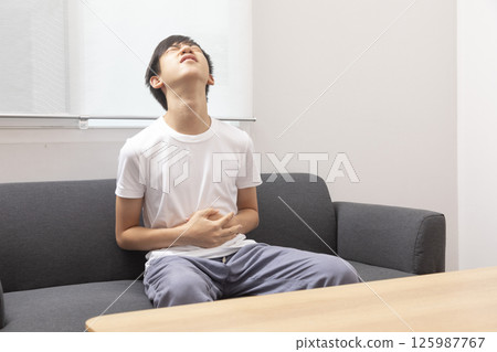 eautiful boy wearing casual  t-shirt at home with hand on stomach because indigestion, painful illness feeling unwell. Ache concept. 125987767