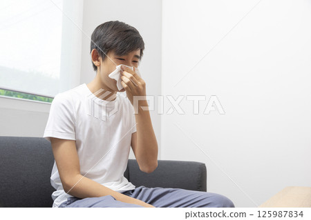 healthcare, rhinitis, people and medicine concept - ill boy with flu lying in bed and blowing his nose at home healthcare, rhinitis, people and medicine concept - ill boy with flu lying in bed and blowing his nose at home 125987834