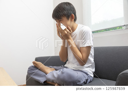 healthcare, rhinitis, people and medicine concept - ill boy with flu lying in bed and blowing his nose at home healthcare, rhinitis, people and medicine concept - ill boy with flu lying in bed and blowing his nose at home 125987839