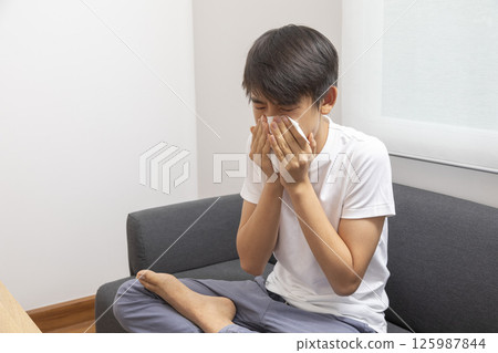 healthcare, rhinitis, people and medicine concept - ill boy with flu lying in bed and blowing his nose at home healthcare, rhinitis, people and medicine concept - ill boy with flu lying in bed and blowing his nose at home 125987844