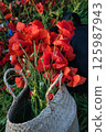 A basket filled with vibrant red poppies sits on a lush green field, surrounded by the beauty of nature.  125987943