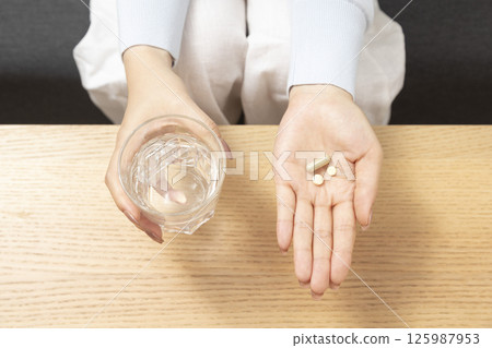 Healthcare treatment supplements. Handful of white round pills in female patients palm woman arm holding heap of small round meds and glass of water before taking medication Healthcare treatment supplements. Handful of white round pills in female patients palm woman arm holding heap of small round meds and glass of water before taking medication 125987953