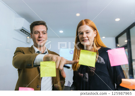 Business people holding pen and put sticky notes on glass wall in office Business people holding pen and put sticky notes on glass wall in office 125987965