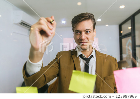 Business people holding pen and put sticky notes on glass wall in office Business people holding pen and put sticky notes on glass wall in office 125987969